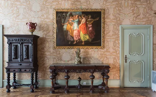 Wnętrze zamku Książ — sala z wzorzystą tapetą, rzeźbioną ciemną szafą, stołem, obrazem w złotej ramie i jasnymi drzwiami
